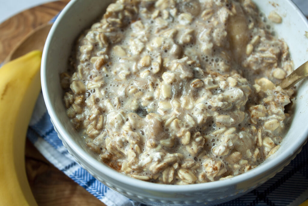 vegan oatmeal with bananas and cinnamon in a white bowl with a spoon and banana on the side. 