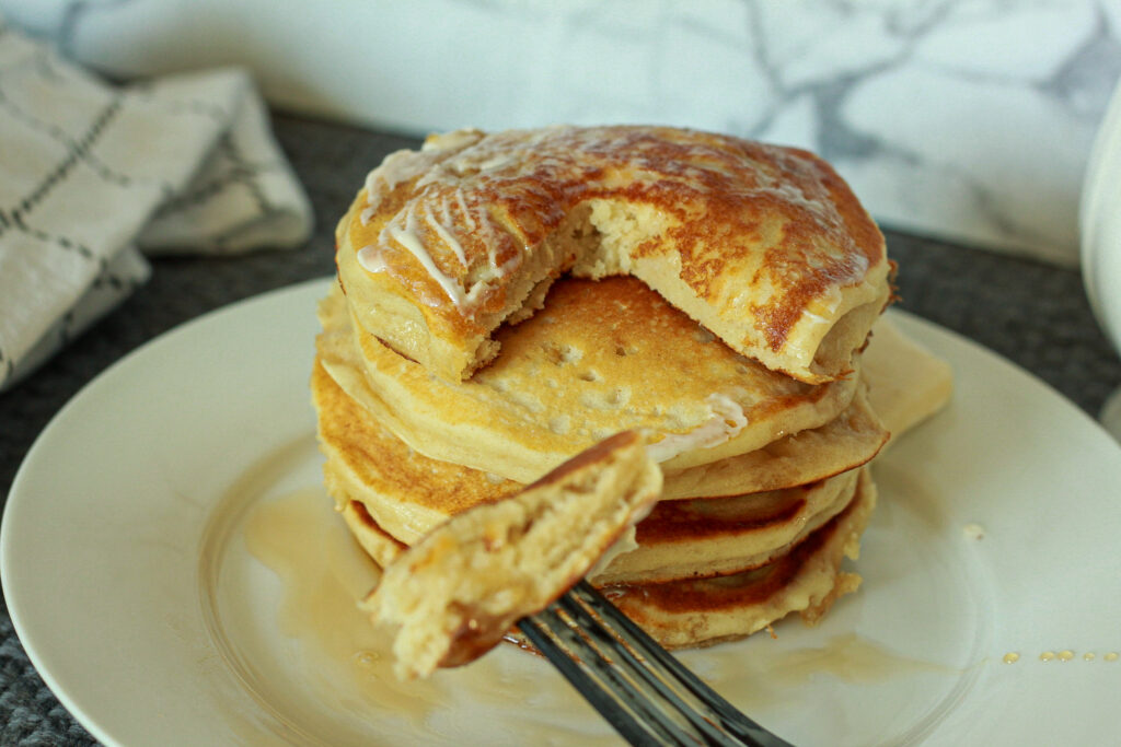 fluffy vegan pancake stack with a bite sitting on a white plate. 