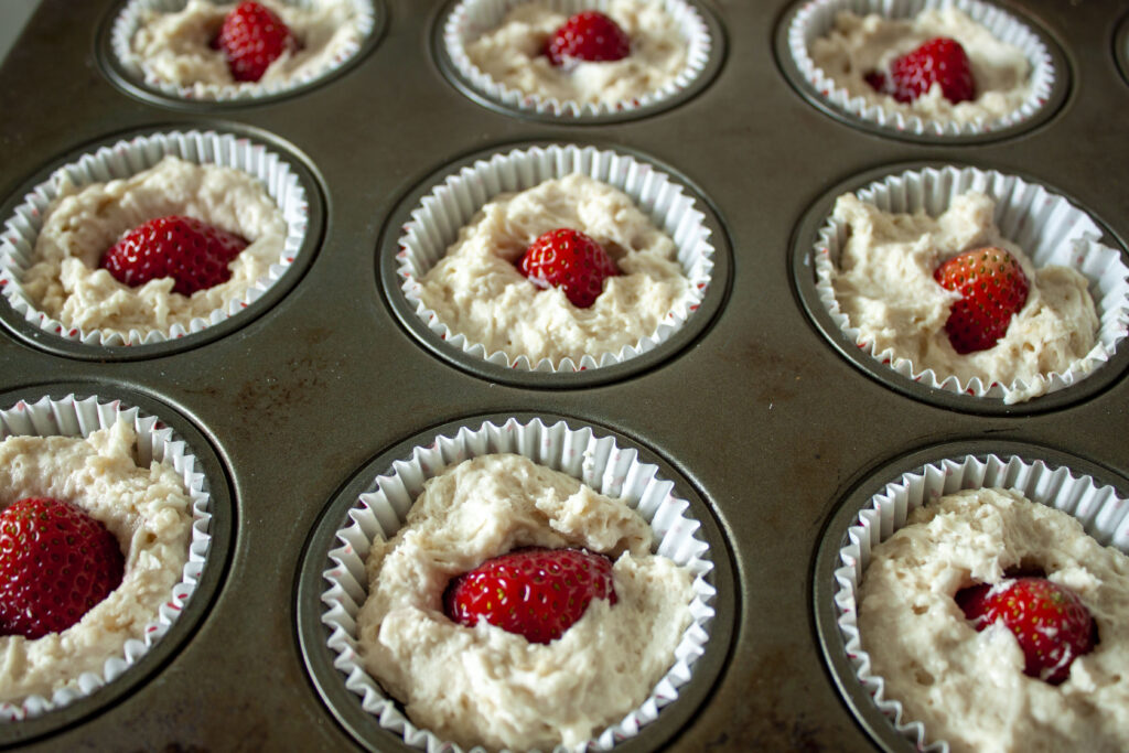 precooked  vegan strawberry shortcake cupcakes in the cupcake liner with the strawberry shoved in the dough. 