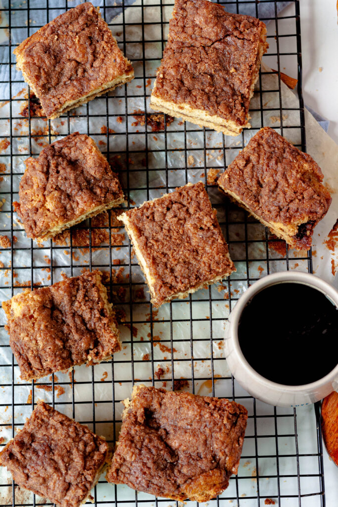 vegan coffee cake squares on a black wire rack with a coffee cup on the rack.
