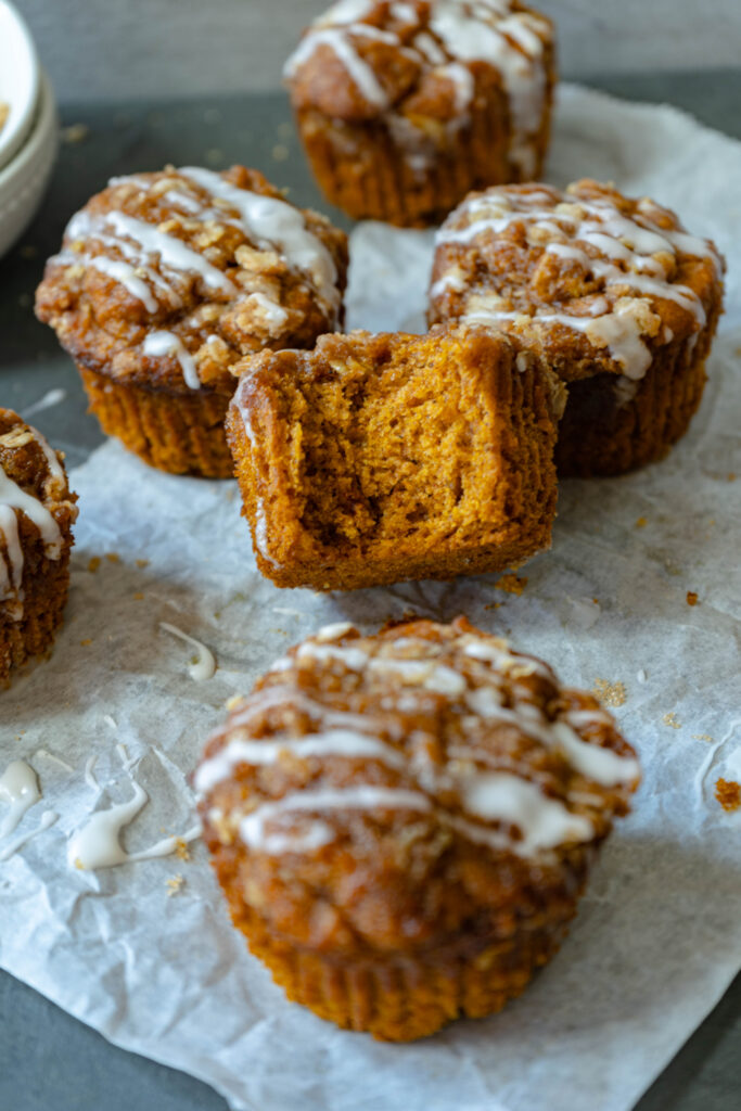 vegan pumpkin spice muffins on a white sheet with one bite taken out of the main one.