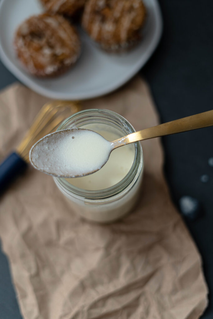 vegan buttermilk on a spoon with the mason jar full of vegan buttermilk underneath it. 