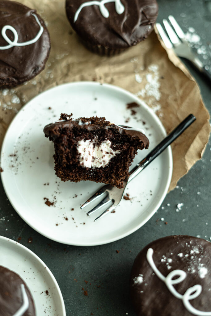 vegan hostess cupcake cut down the middle so you can see the filling on a white plate with a mini fork. 