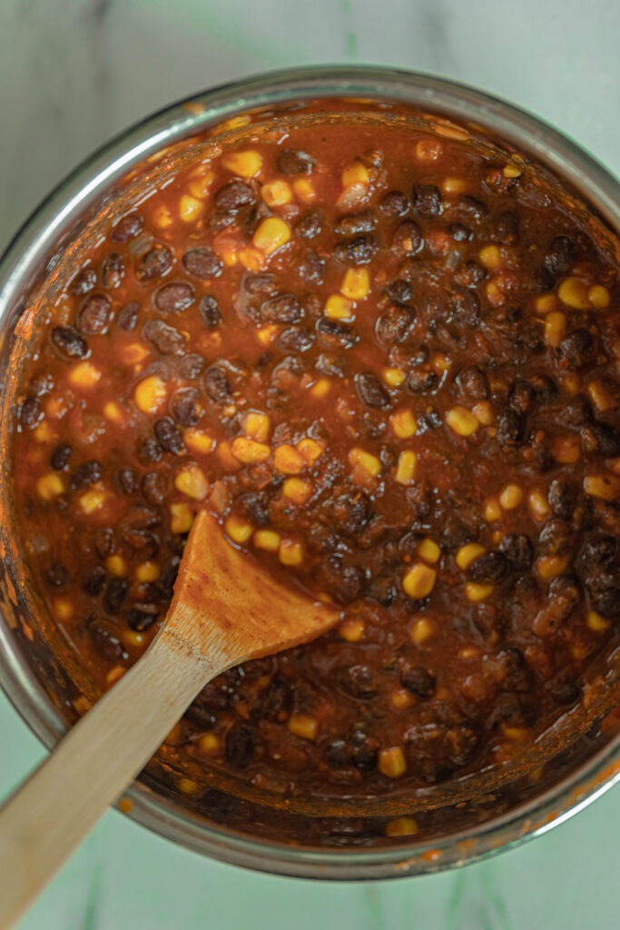 precooked vegan black bean chili in an instant pot with a big wooden spoon for stirring. 