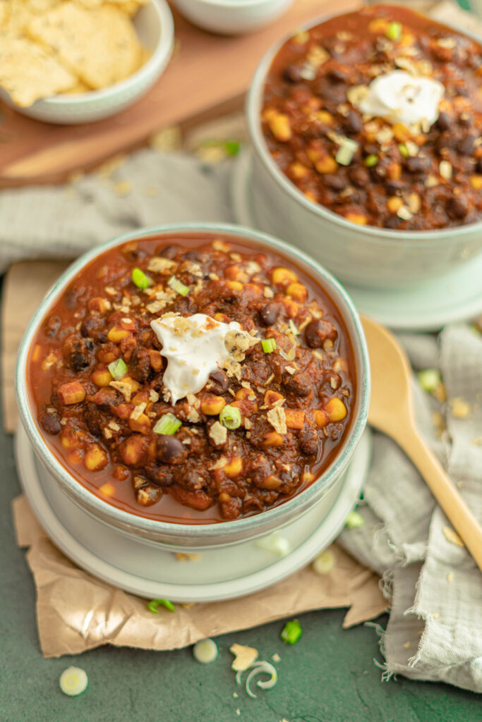 vegan black bean chili recipe with sour cream in a bowl on a plate with a wooden spoon on the side.