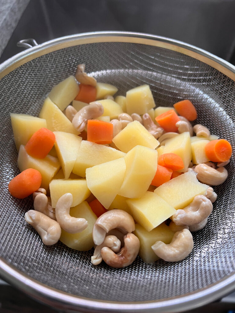 strained vegan nacho cheese boiled potatoes, carrots, and cashews in a metal strainer. 