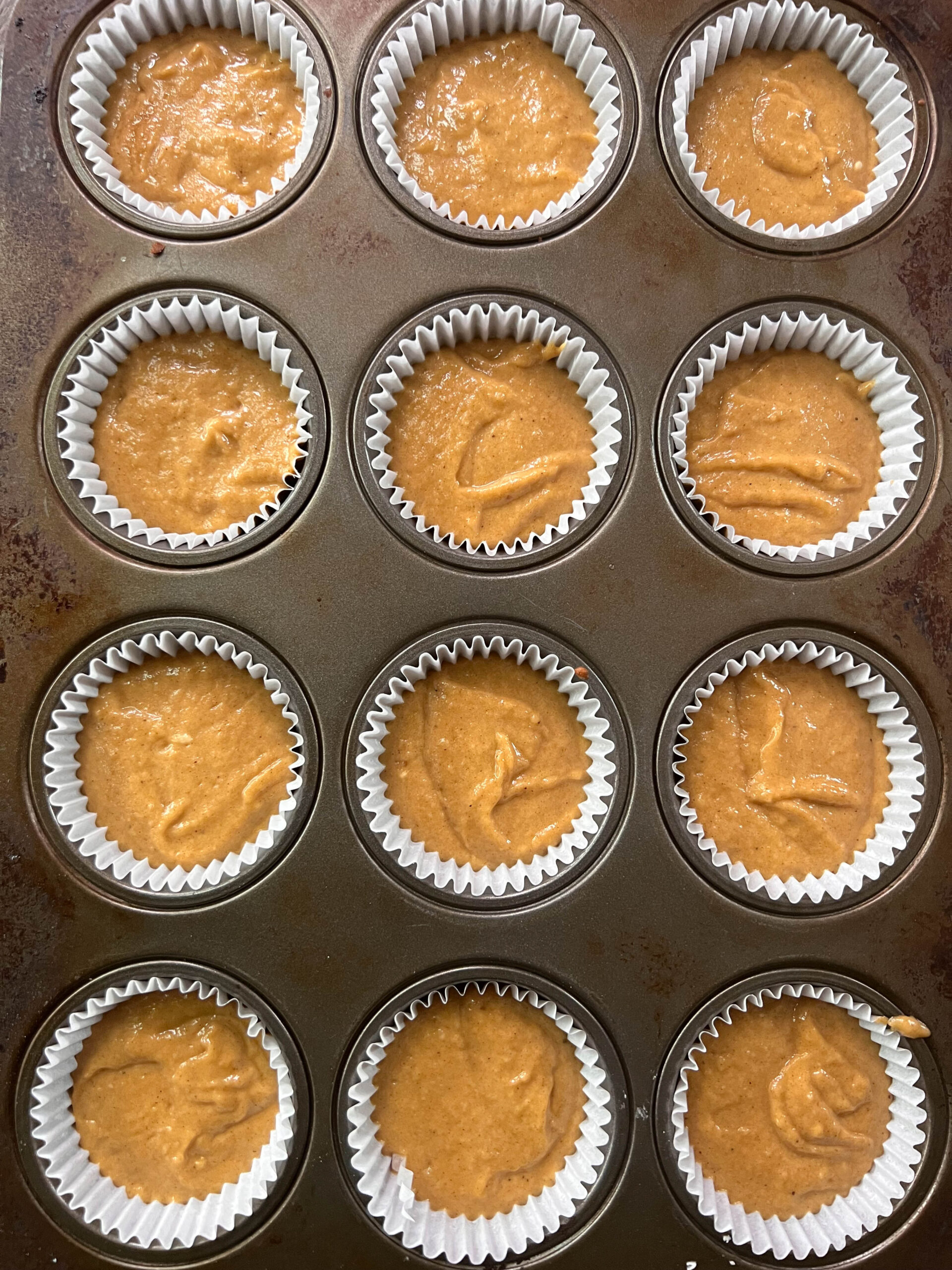 Uncooked vegan pumpkin cupcakes in liners in the cupcake tin. 