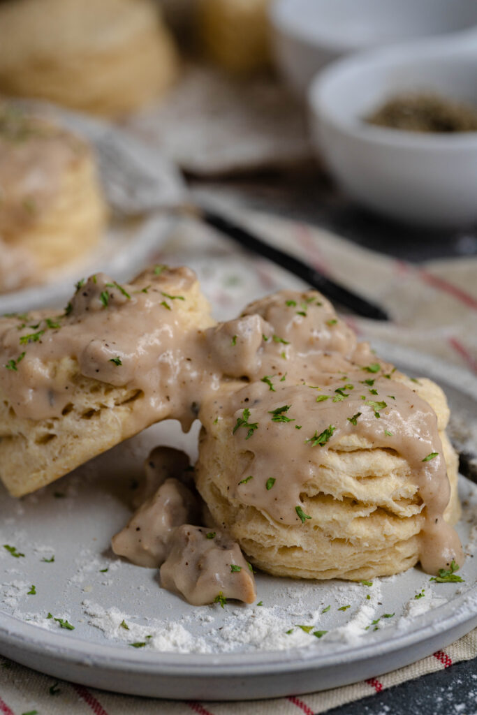 two  biscuits with gravy on top on a white plate. 