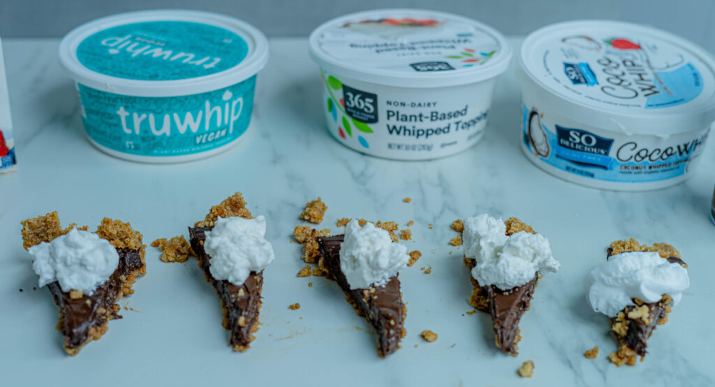 vegan whipped cream options all on a tiny slice of chocolate pie with the containers in the background on a white surface. 