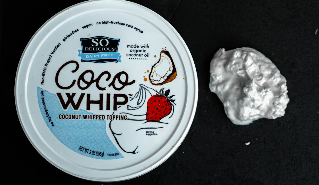 vegan So delicious Coco whip container with a dollop of whipped cream on a black background. 