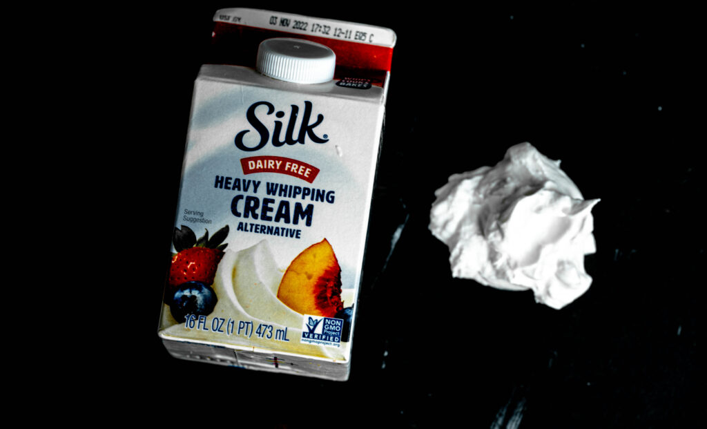 vegan silk whipping cream container with a dollop of whipped cream on a black background. 