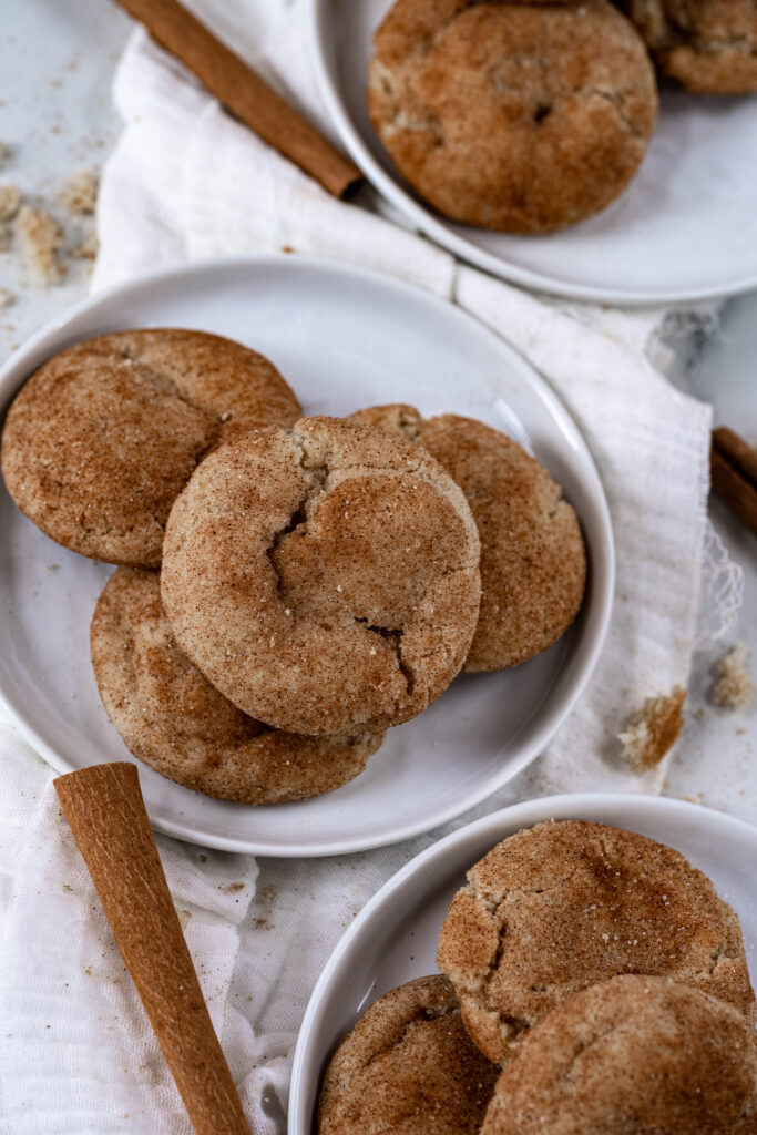 vegan snickerdoodles piled on a white plate with half a matching plate showing. 