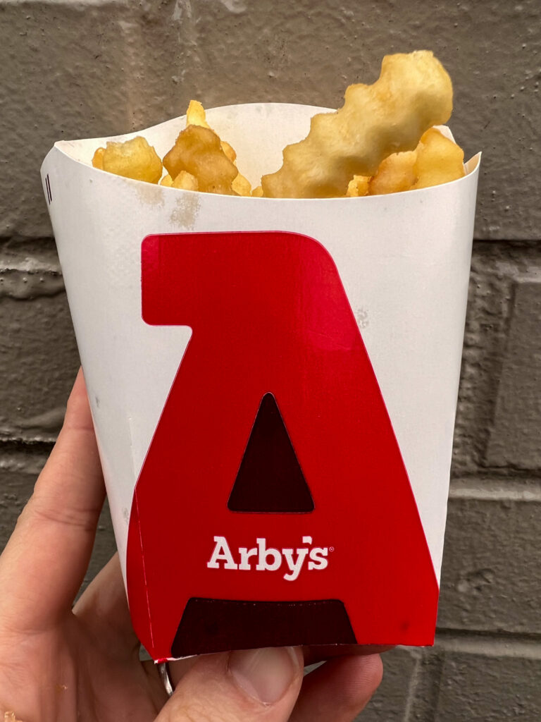 vegan crinkle fries vegan arbys held up with a brick background. 