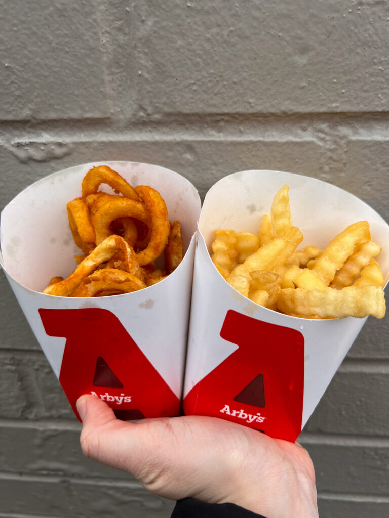 vegan arbys options the curly fries and regular fries being held up together with a brick background. 