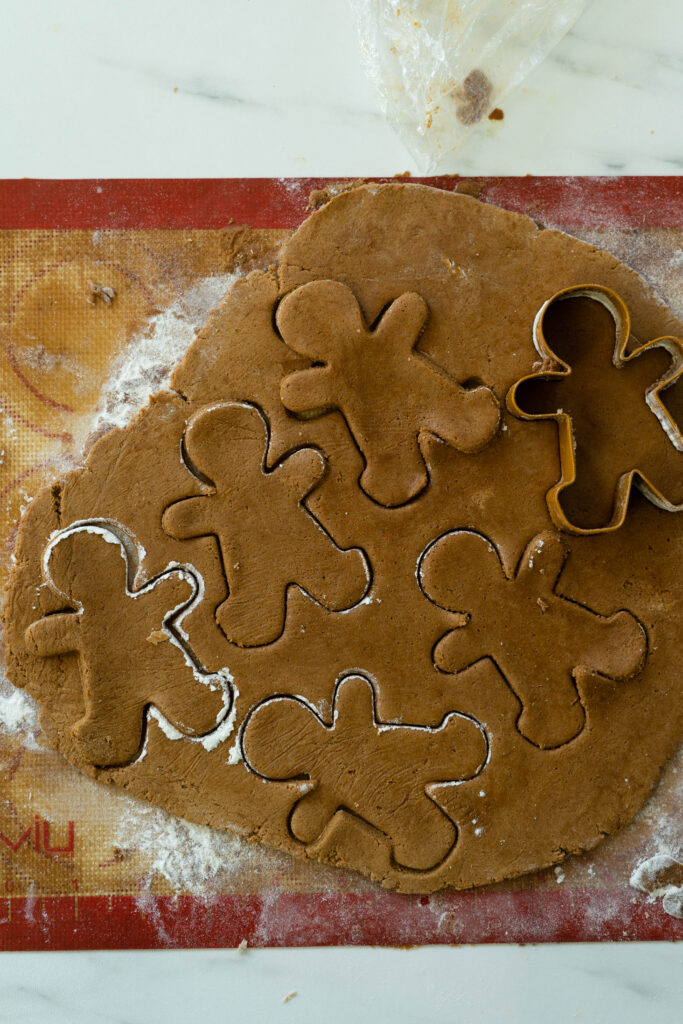 cutting out vegan gingerbread men on a sheet of cookie dough with a cookie cutter.