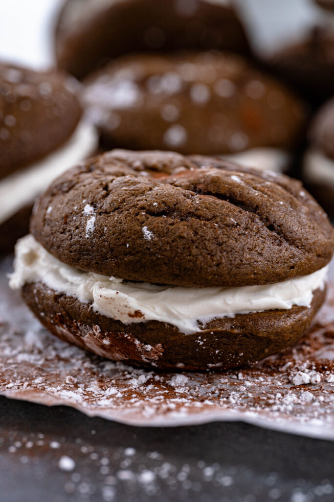 single vegan whoopie pie  on a sheet covered with powdered sugar and cocoa powder. 