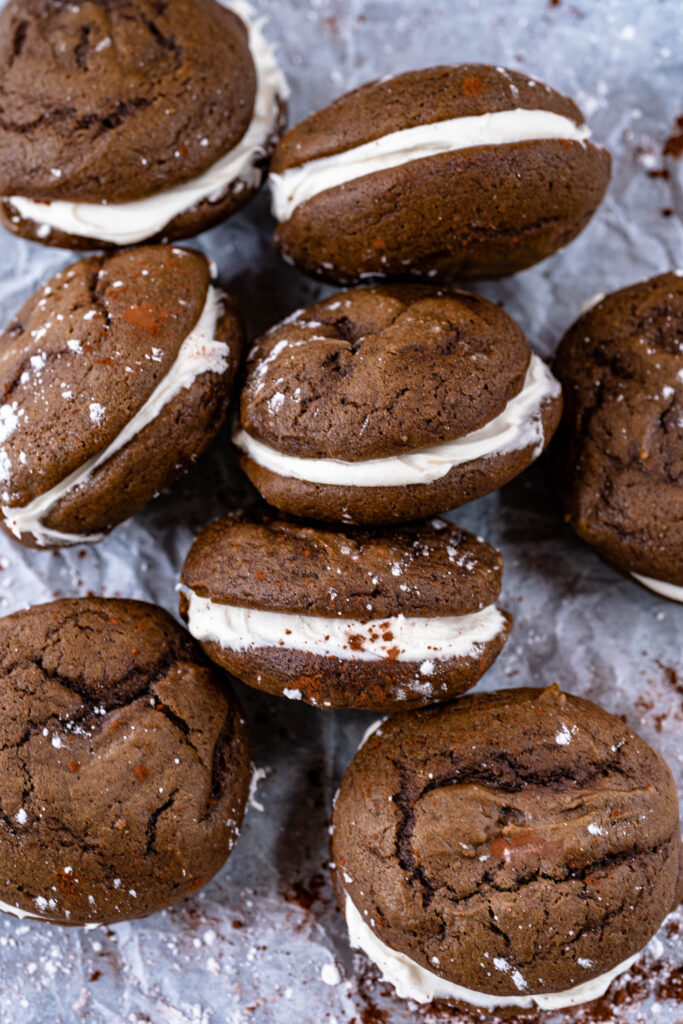 vegan whoopie pies laying on a white background dusted with powdered sugar in different orientations. 