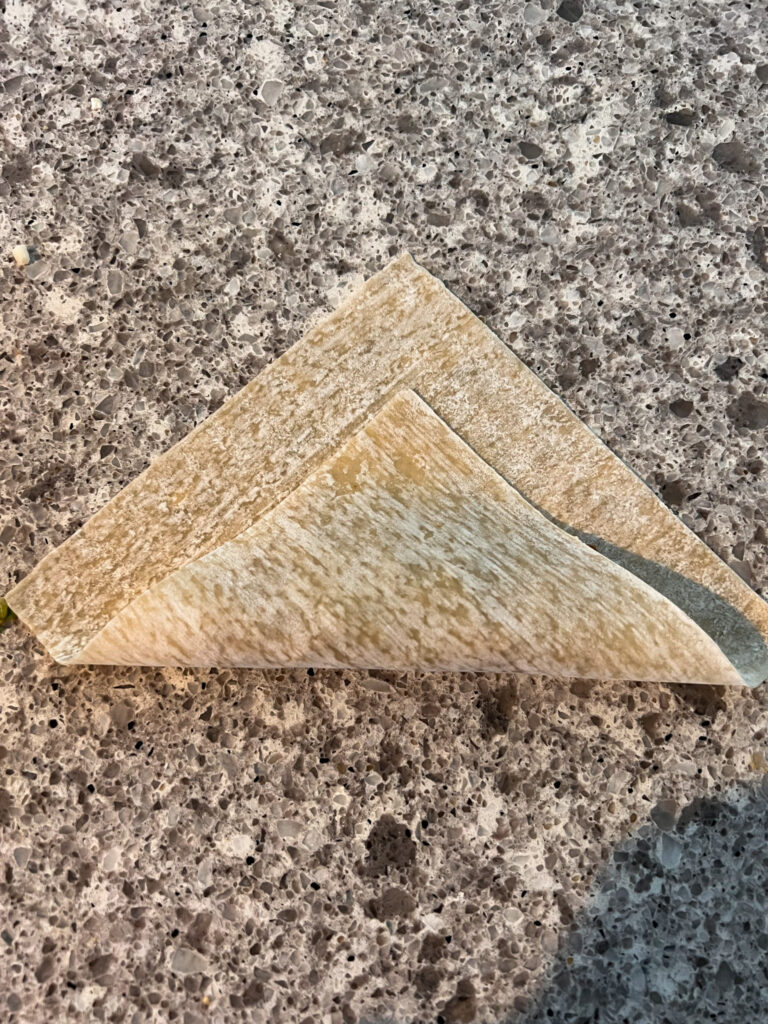 folding the egg roll wrapper in half on a busy granite background. 