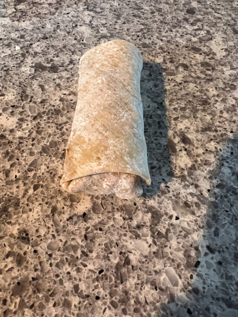 Vegan egg roll  all rolled up like a burrito on a busy granite background.