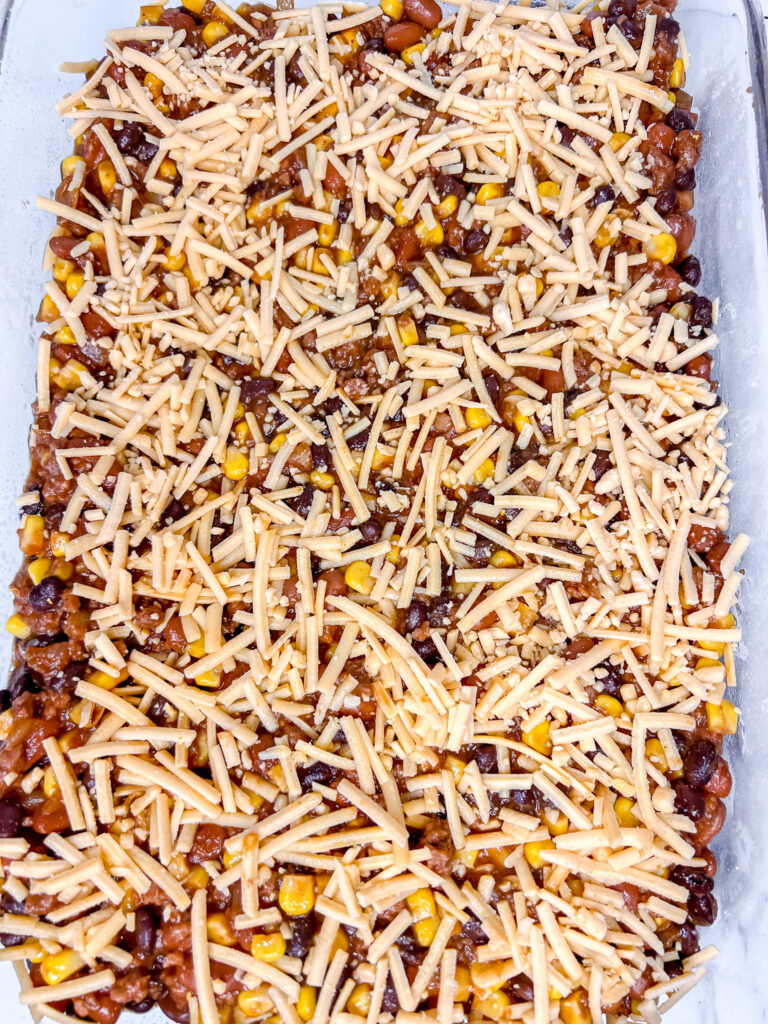 vegan frito pie in a 9x13 pan with vegan cheese on prebaked close up shot. 