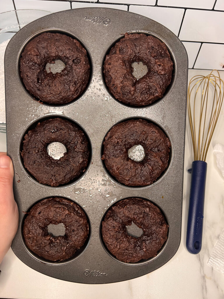 Baked vegan donuts in the donut pan on the counter with a whisk to the side.