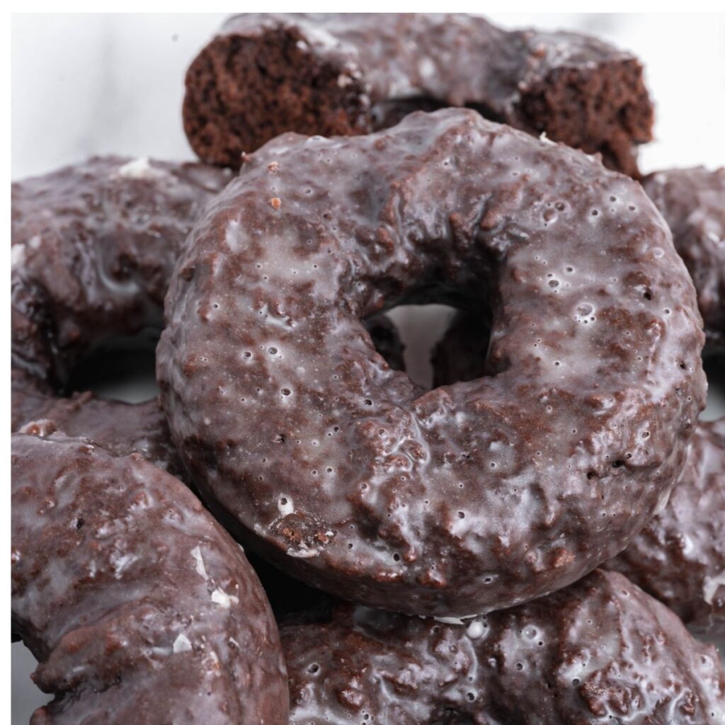 vegan baked chocolate donuts piled on top of each other on a white background. 