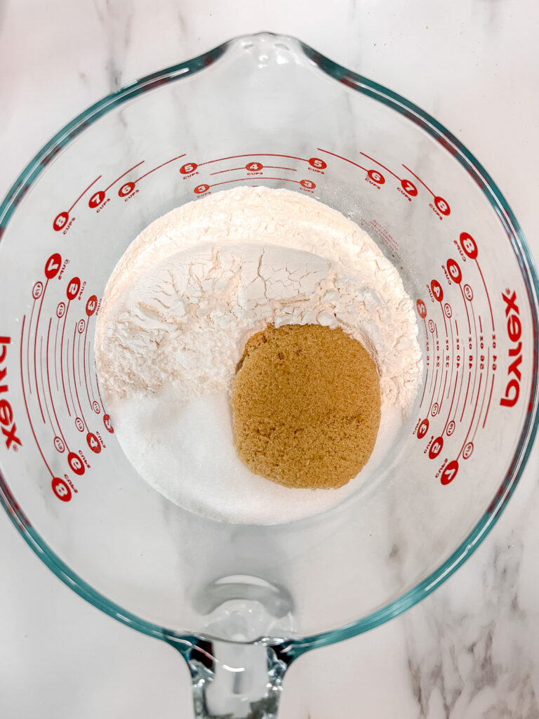 A glass bowl with flour, brown sugar and sugar in it not mixed. 