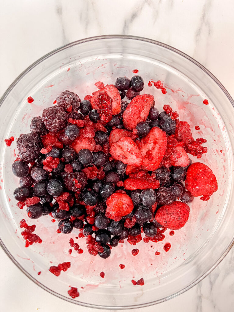 Frozen mixed berries in a glass bowl on a white background. 