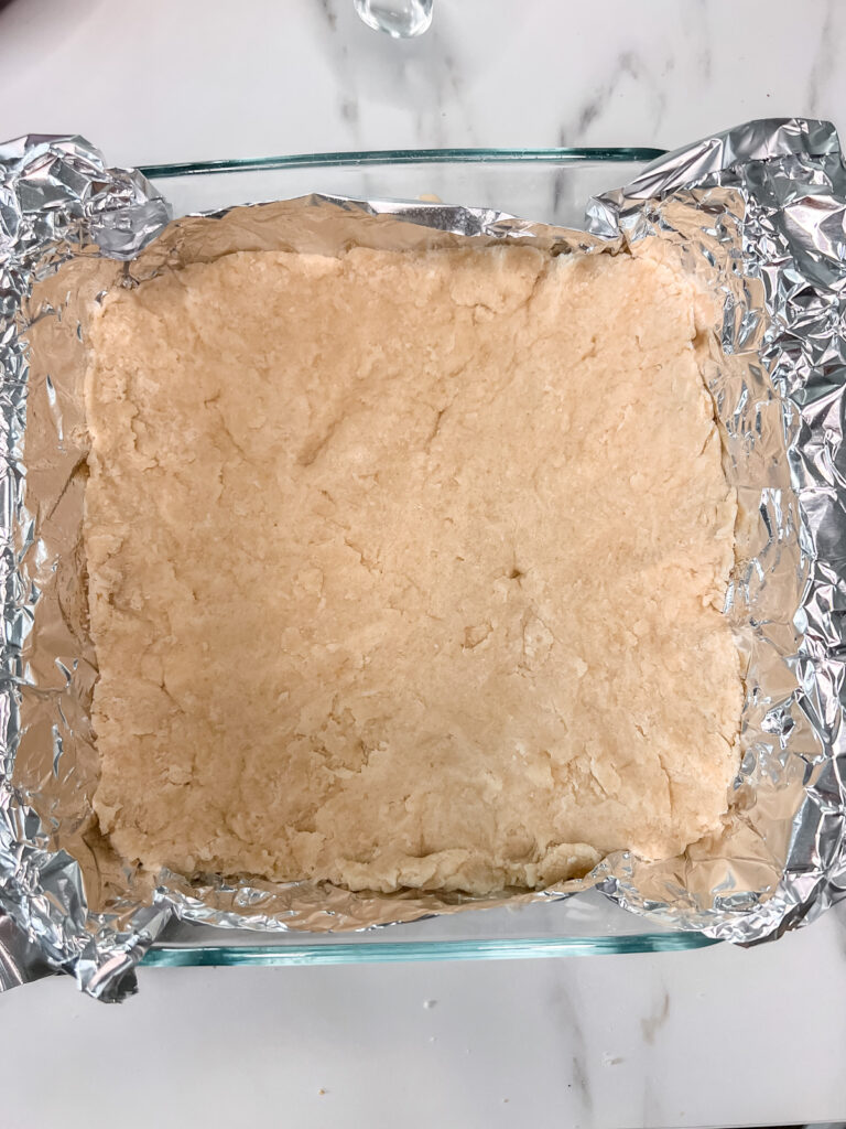 A 8x8 glass pan with foil and the dough on the bottom .