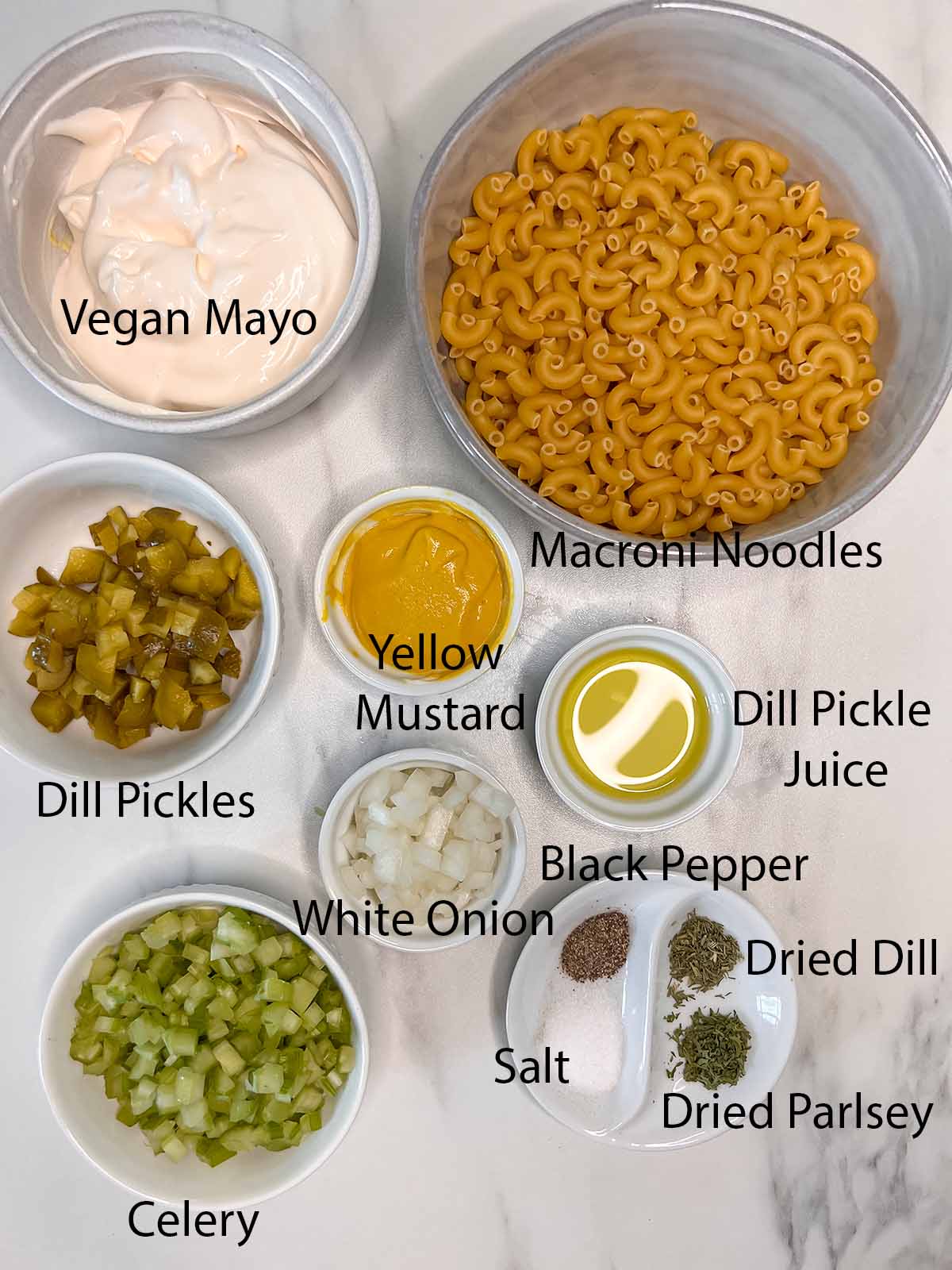 vegan macaroni salad ingredients in small bowls and a marble background. 