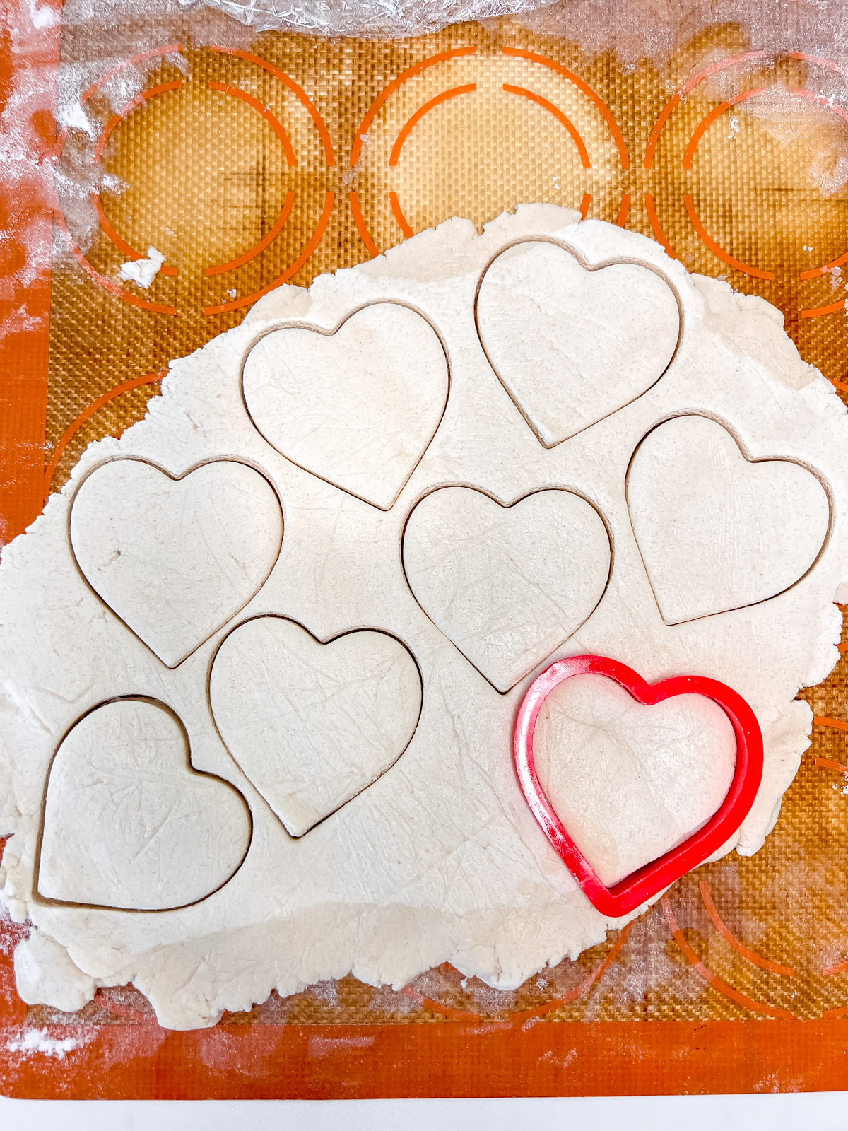cookie dough rolled out flat on a silpat with hearts cut out with a heart cookie cutter. 