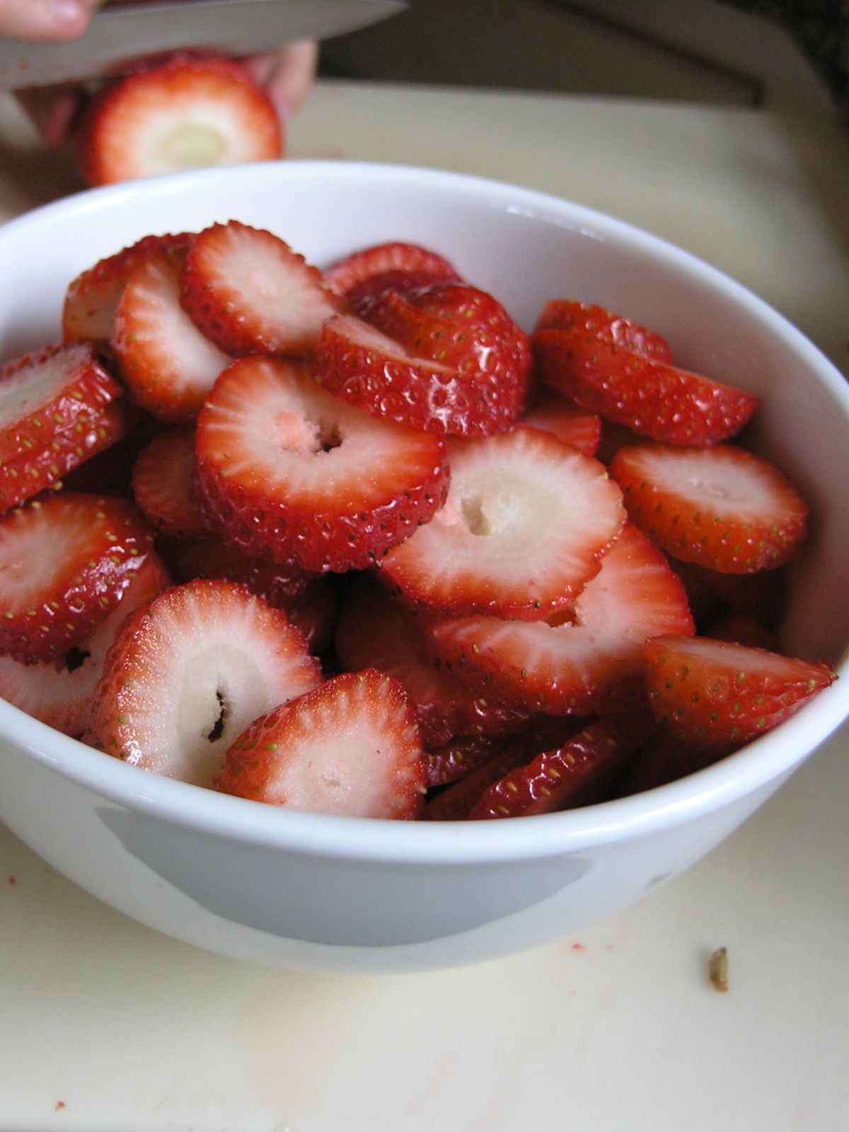 A white bowl filled with cut strawberries on a white background. 