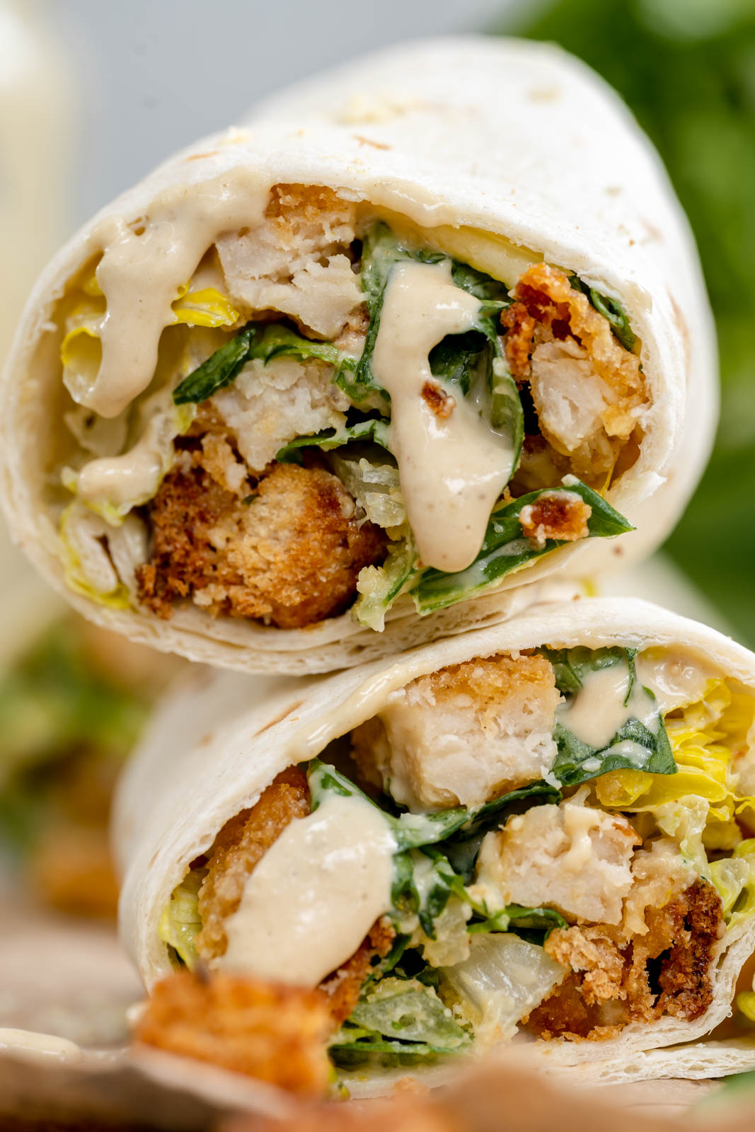 A close up shot of vegan Caesar salad wraps cut in half on top of each other with sauce dripping down. 