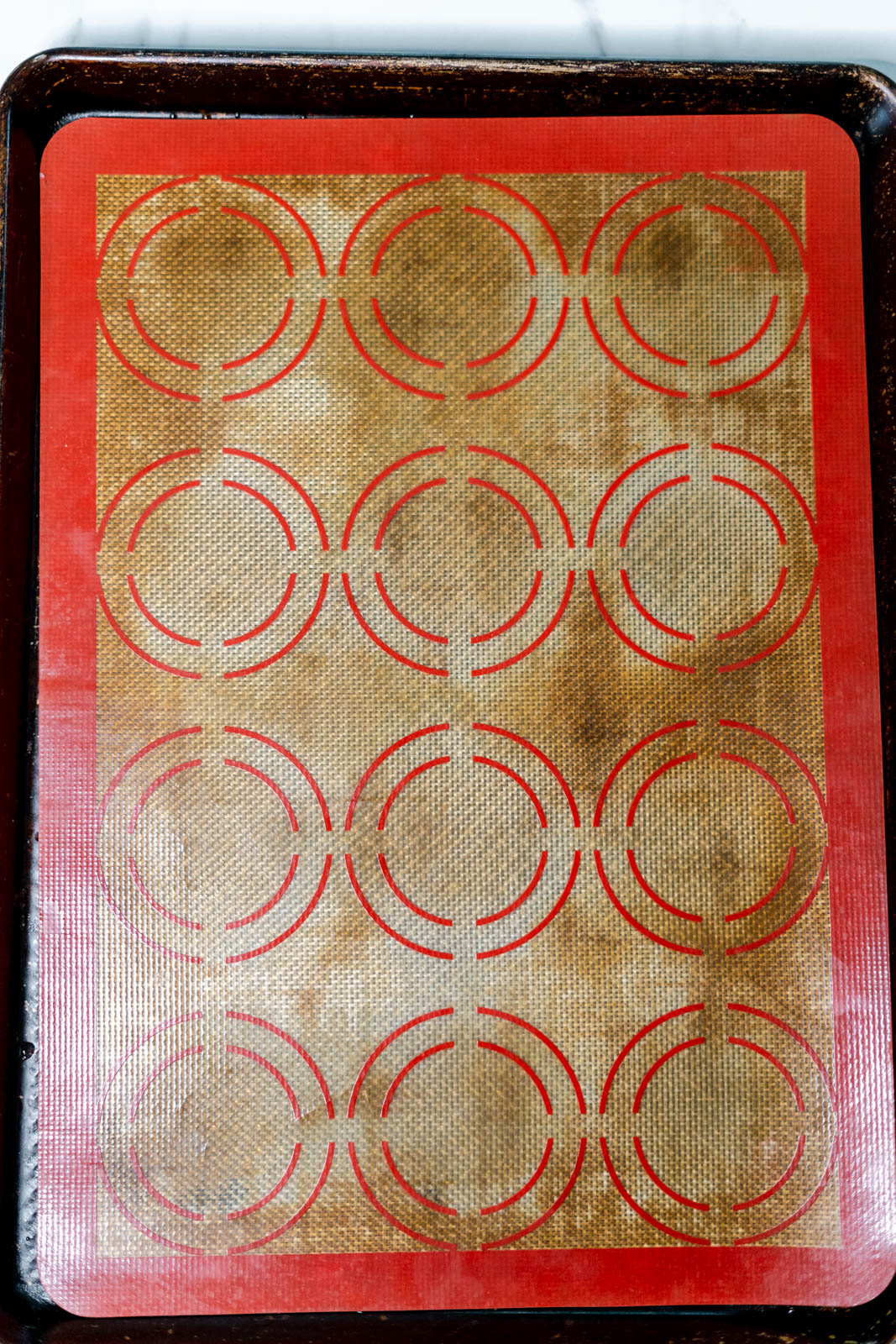 Cookie sheet with a red and brown Silpat with circles on it. 