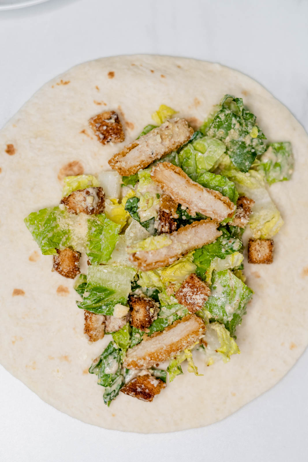 Vegan caesar salad mix on a tortilla before rolling it up on a white background. 