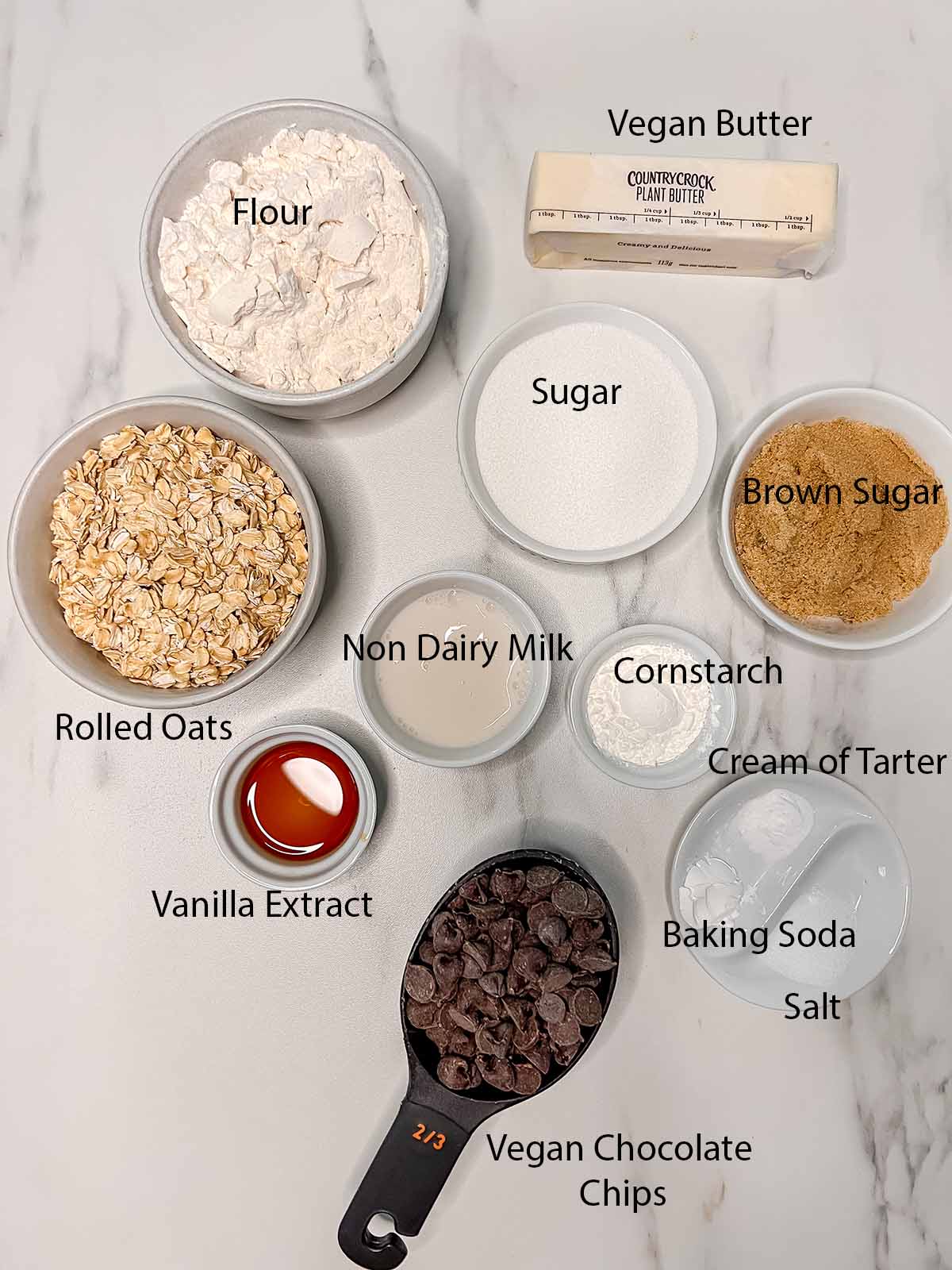 All the vegan chocolate chip oatmeal cookie ingredients in individual containers with black labels. 