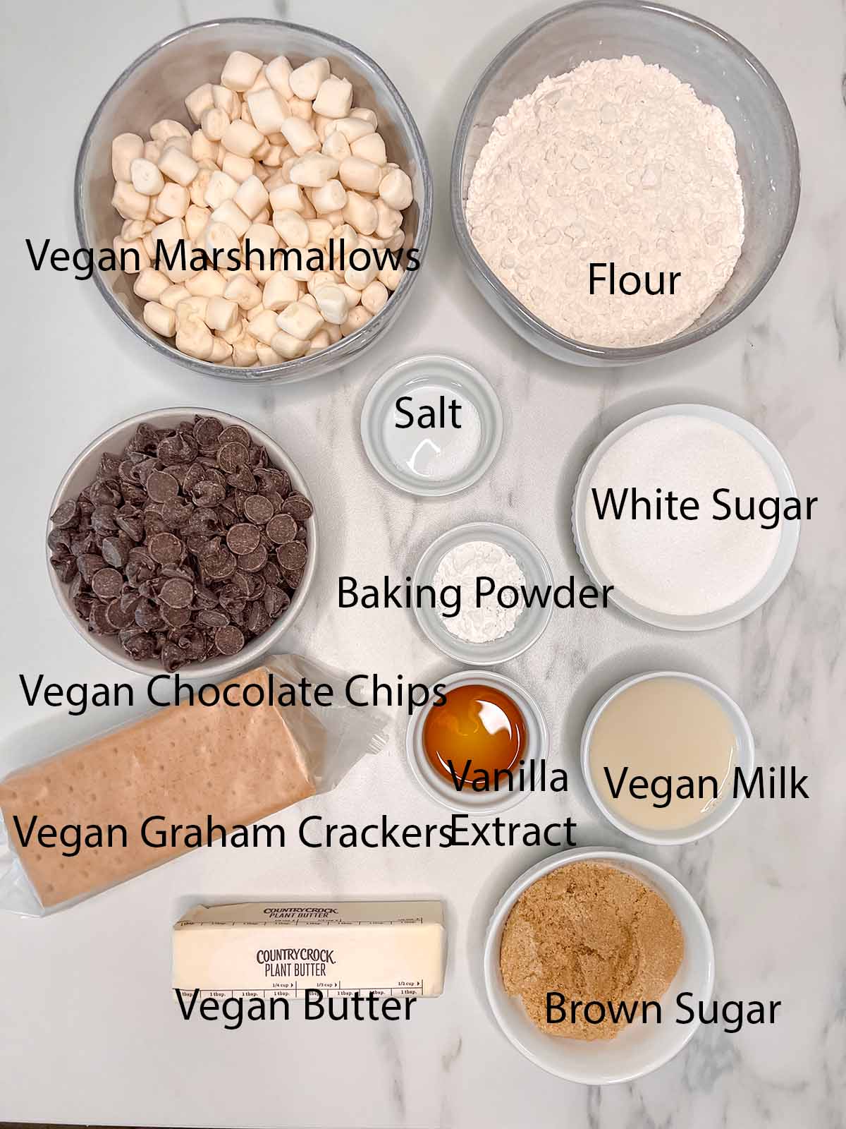 All the ingredients that go into vegan smores bars in small containers with black writing to label them. 