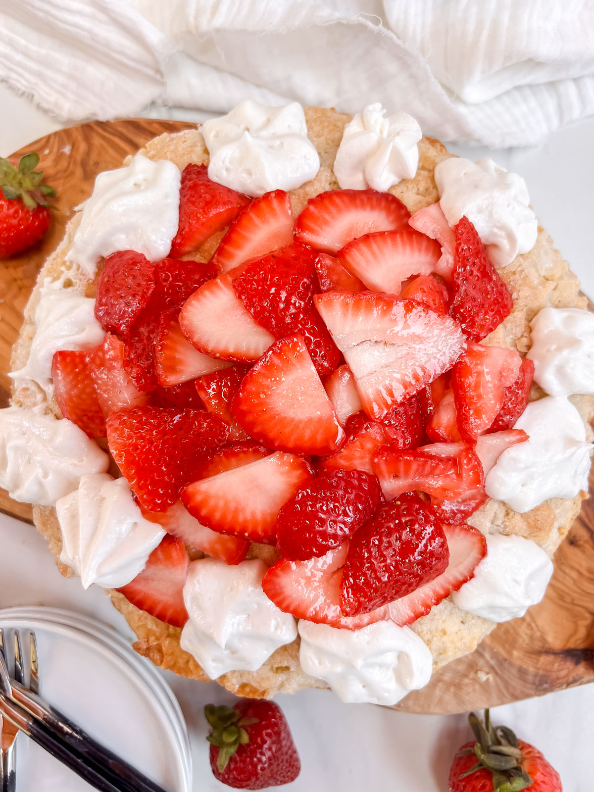 Vegan strawberry shortcake overhead shot with a bunch of sliced strawberries in the middle and whipped cream on the sides on a wood and white background. 