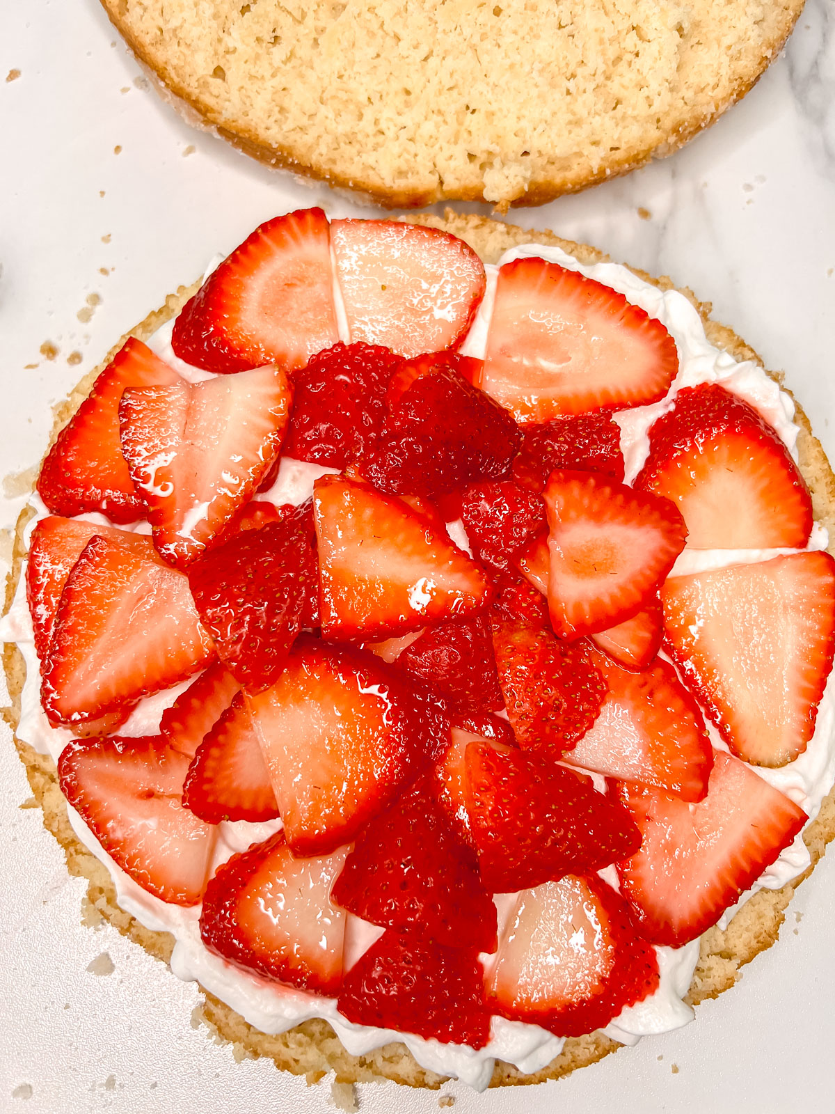 Half of a cake with a layer of whipped cream and sliced strawberries on a marbled background. 