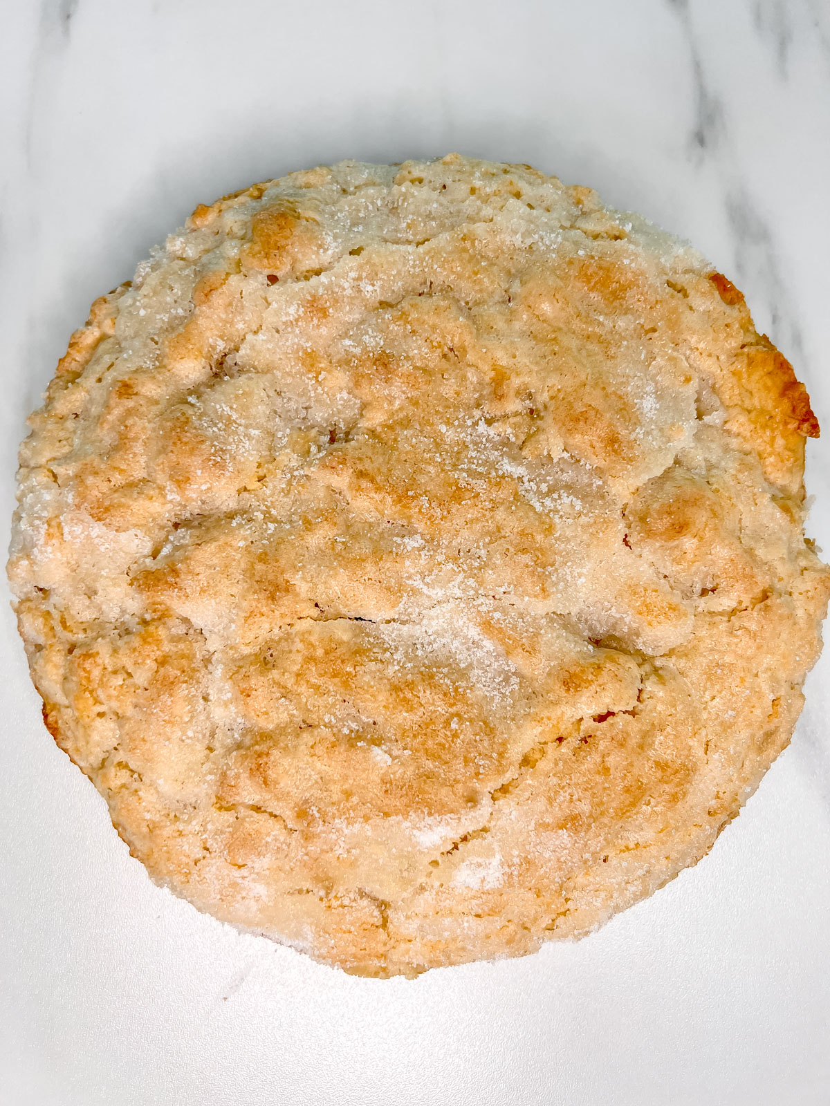 A vegan biscuit round cake with crackles on top on a white marble background. 