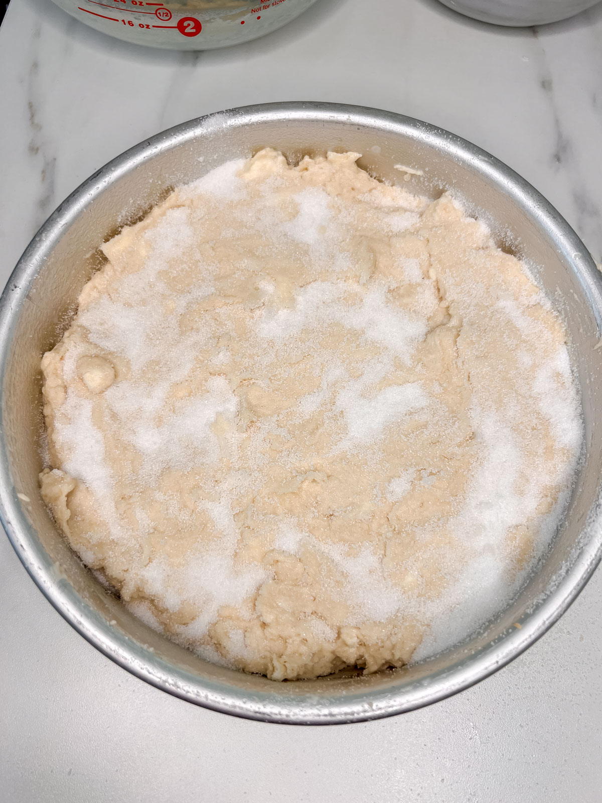 The biscuit cake dough in a metal pan with sugar sprinkled over it on a white background. 