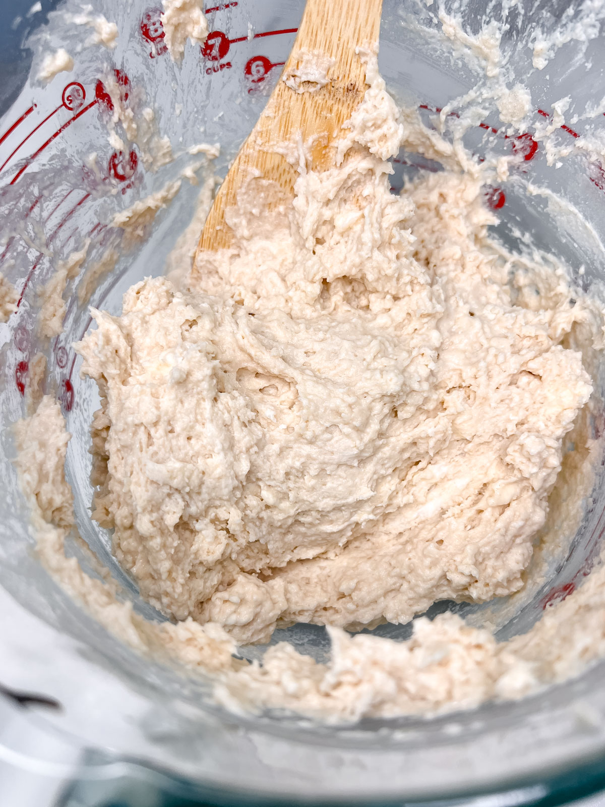 The dough coming together looks like a bit of a wet sticky dough in a glass bowl with a wooden spoon. 