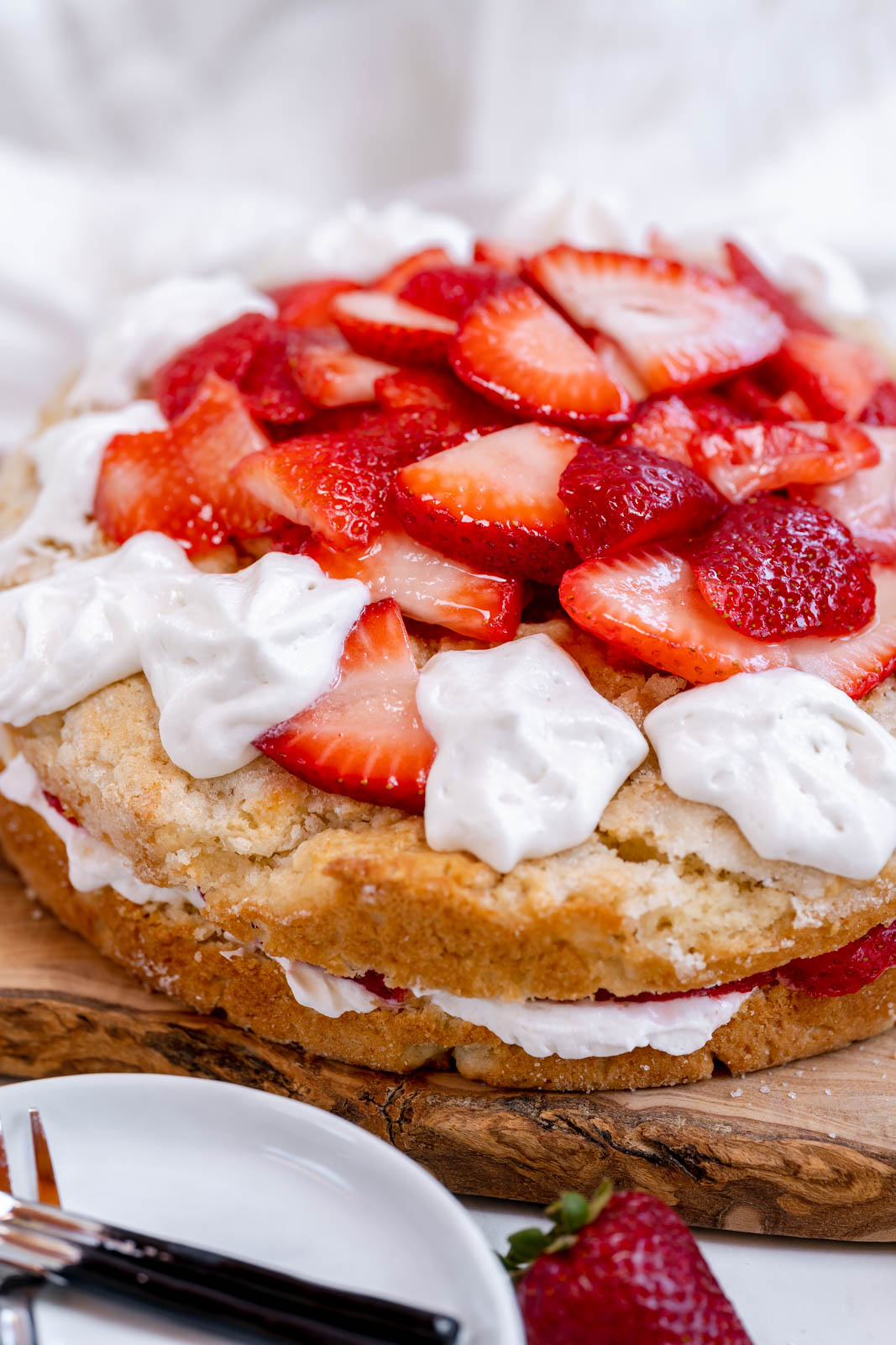 A round biscuit cake with strawberries piled in the middle and dots of whip cream on the edges on a wood table. 