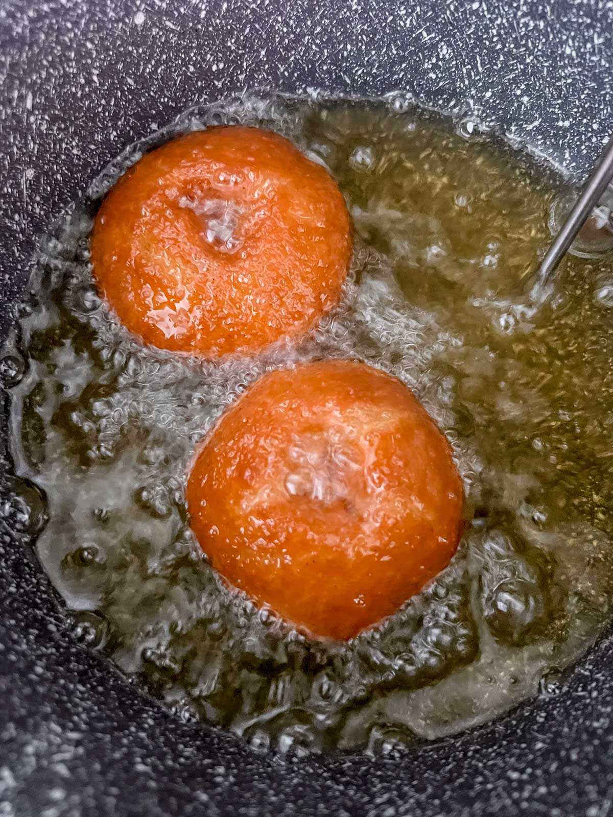 Two vegan apple cider donut frying in oil. 