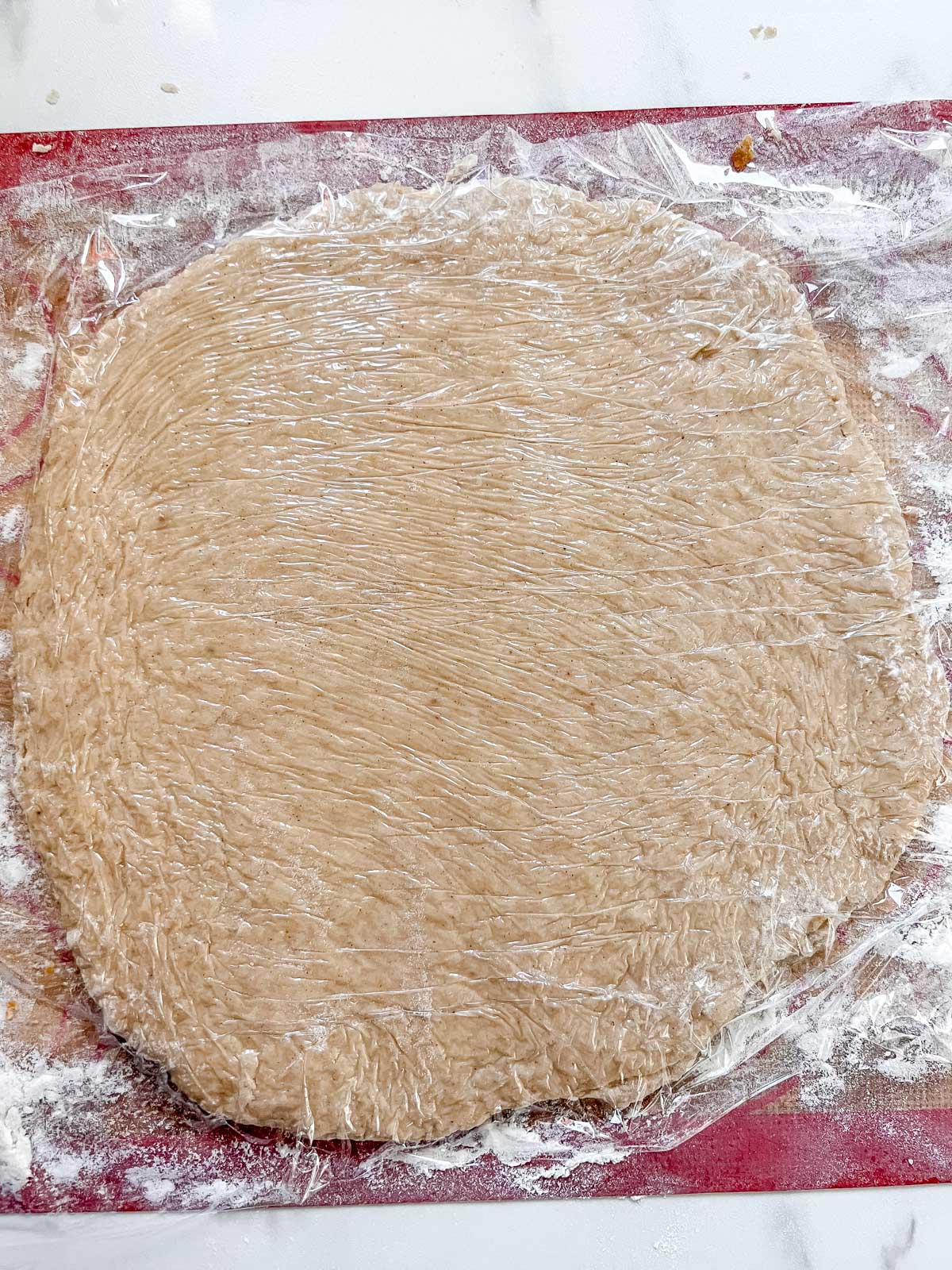 Half the vegan apple cider donut dough on a floured silpat with plastic wrap over the dough rolled out. 