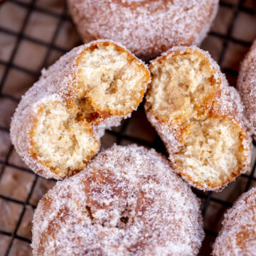 Vegan apple cider donuts on a cooling rack with one donut split in half.