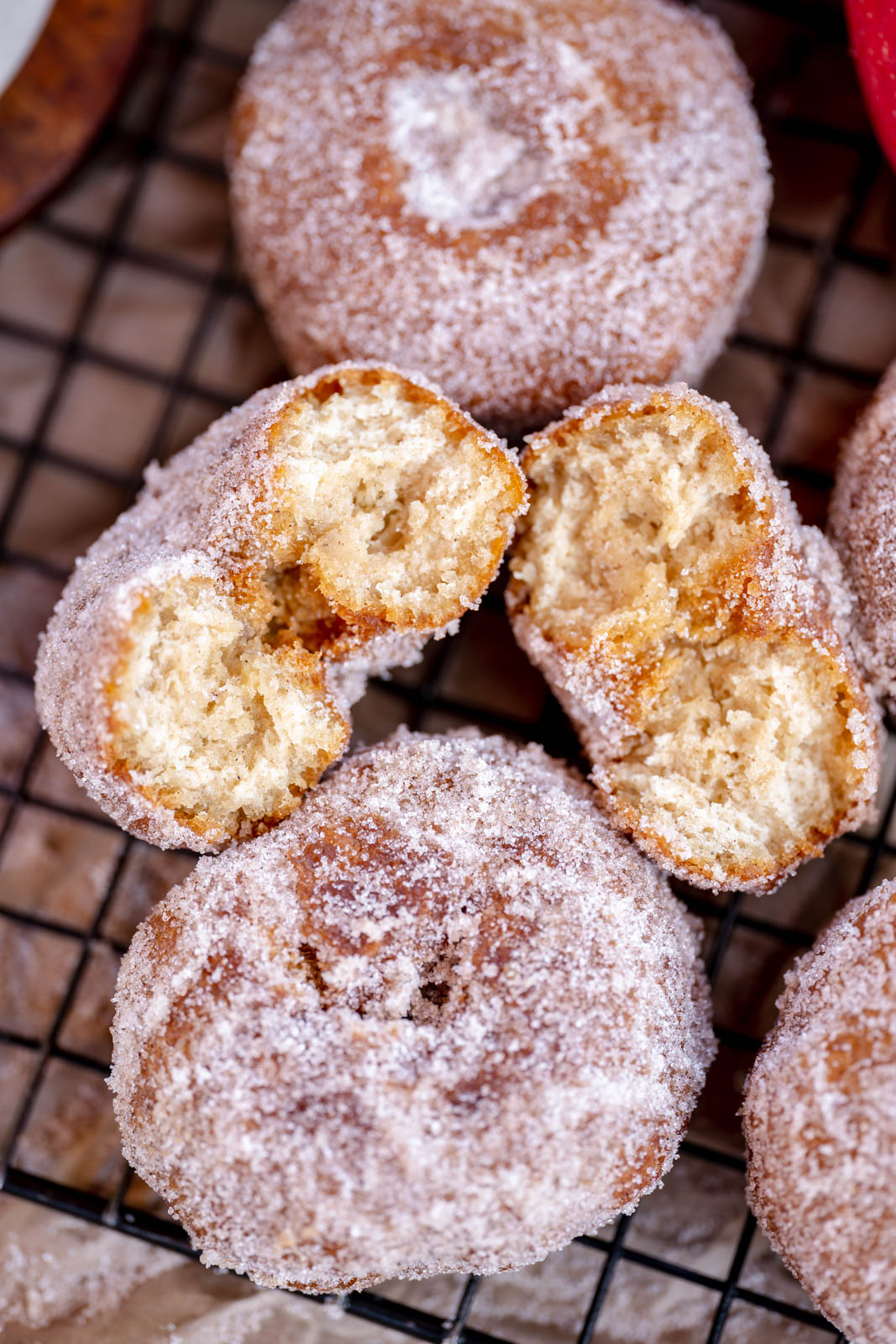 4 vegan donuts two whole ones and one split one to show texture on a black cooling rack. 