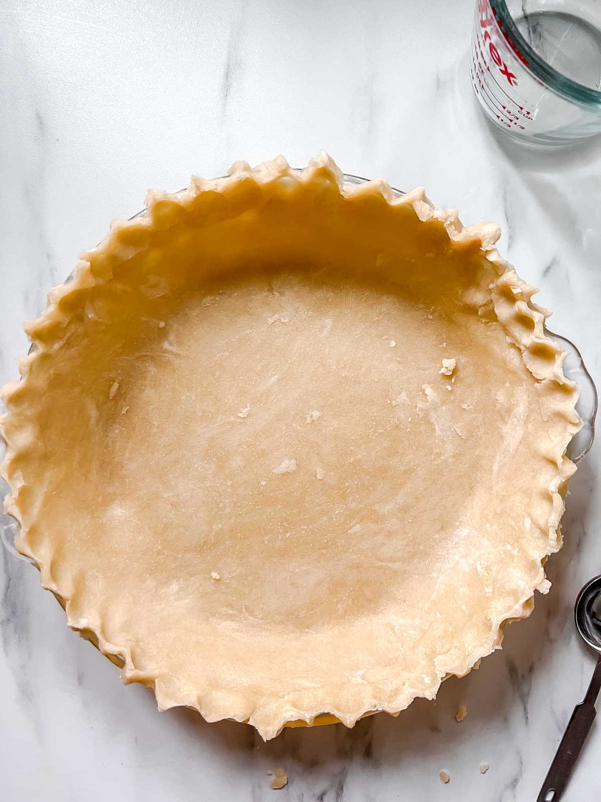Vegan unbaked pie crust in a pie pan on a marble background. 