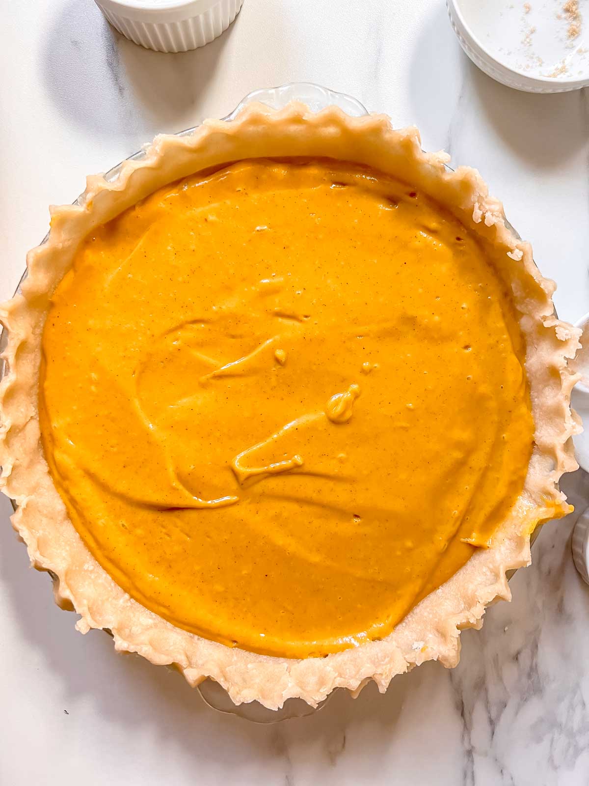 Unbaked vegan pie crust with pumpkin pie filling in it on a marble background. 