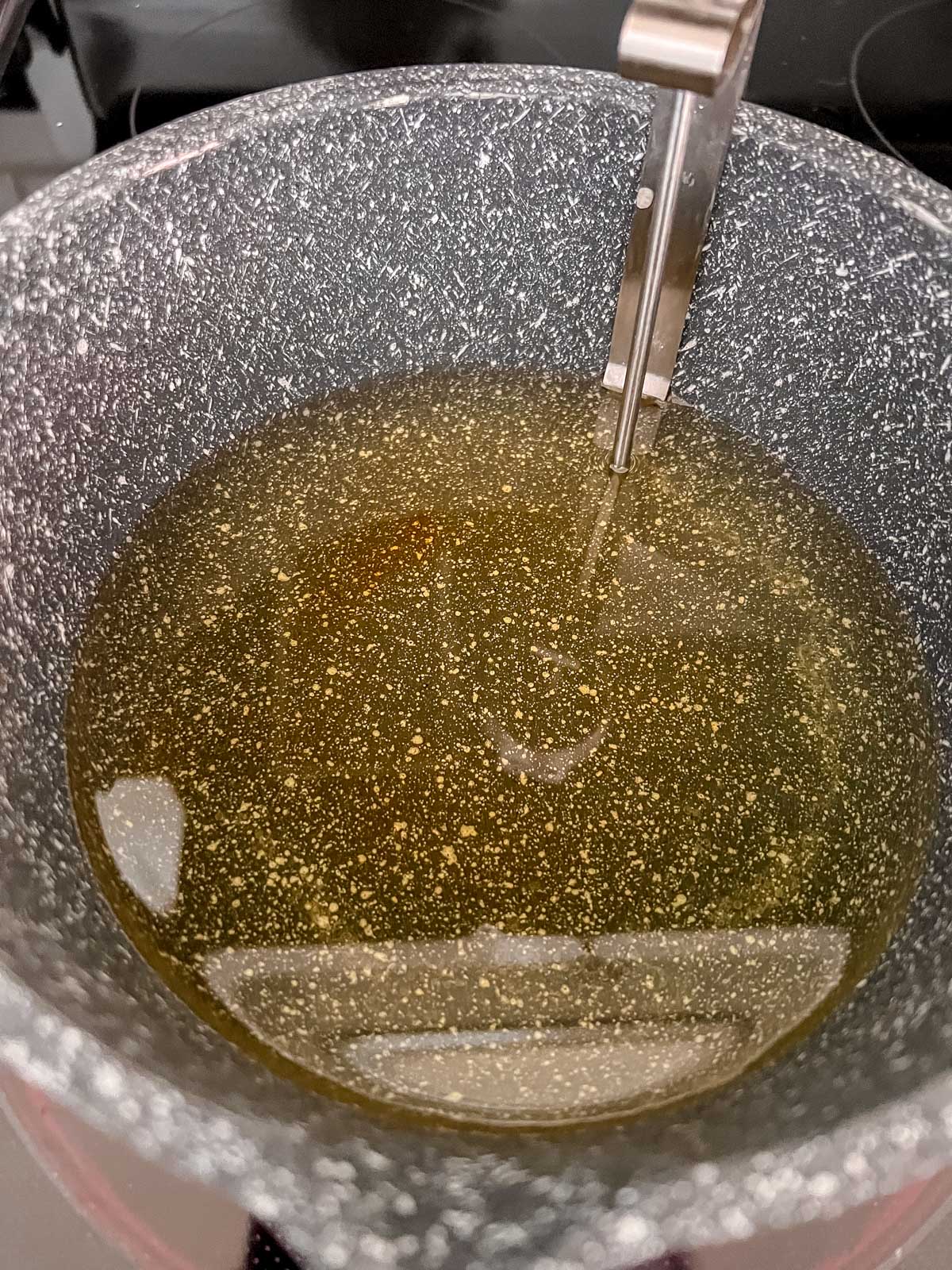 Yellowish oil in a speckled sauce pan with a candy thermometer in it. 